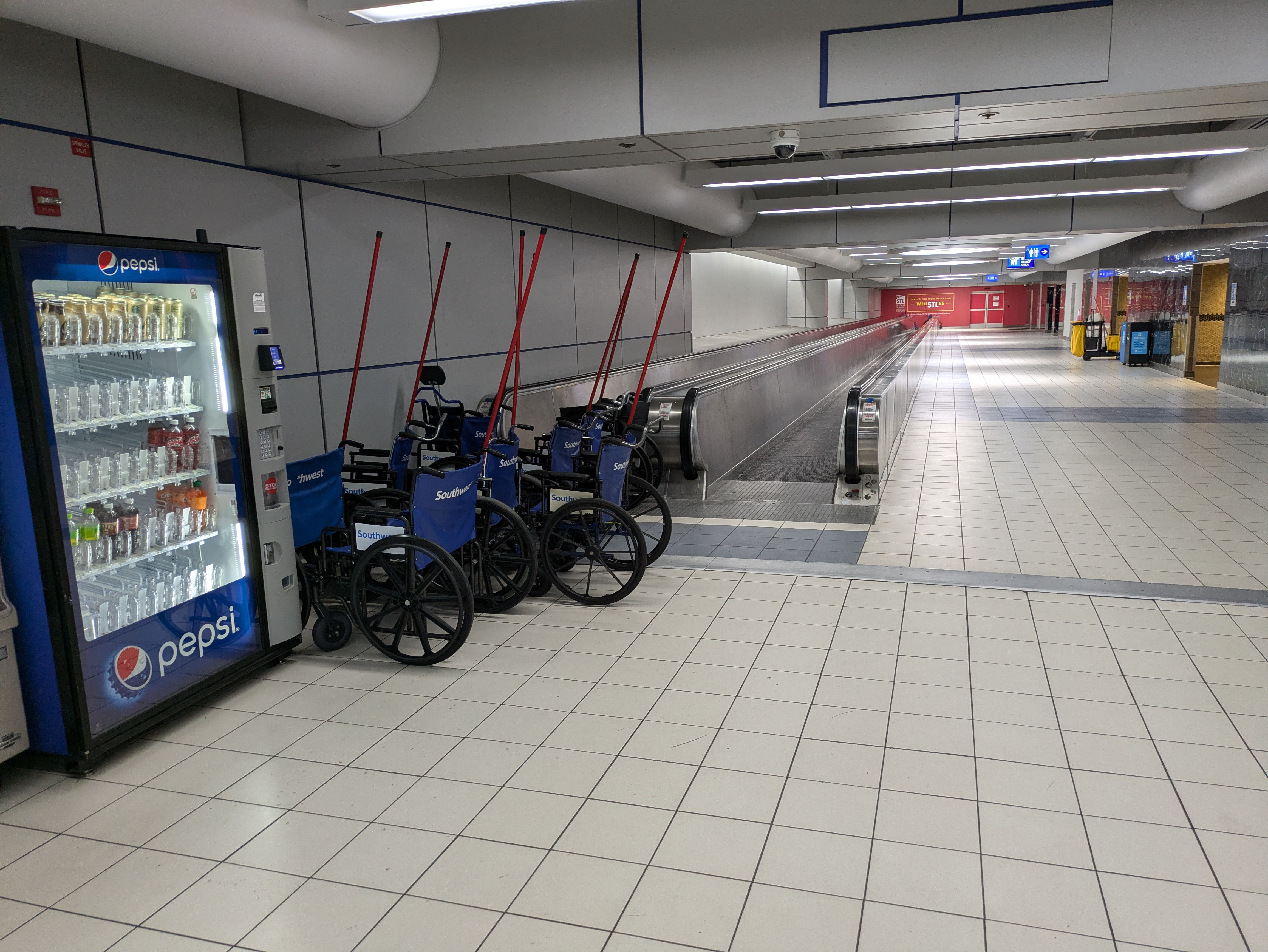 A half-empty vending machine, eight Southwest Airlines-branded wheelchairs, and two unbranded wheelchairs sit at the foot of the moving sidewalk.