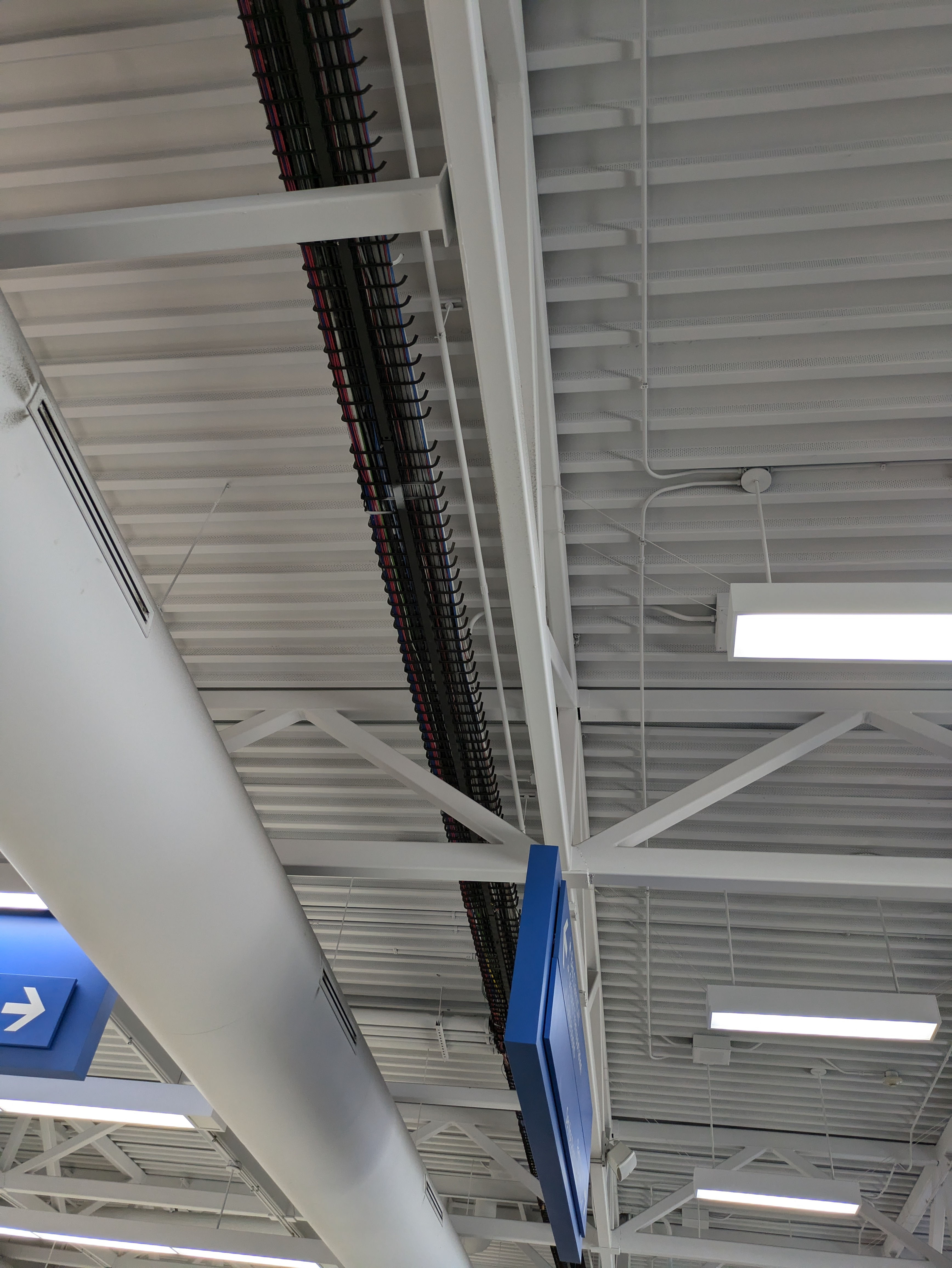 Exposed ventilation equipment, wiring, lighting fixtures, and cable raceways in the ceiling.